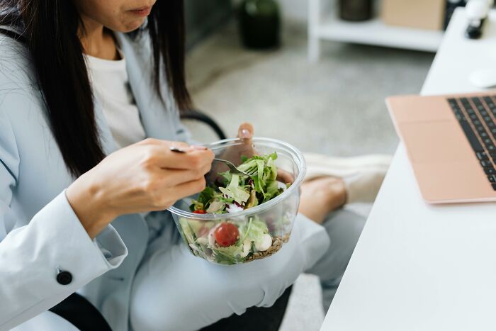 Person in business attire eating a salad at their desk, illustrating workplace rules that can annoy employees.