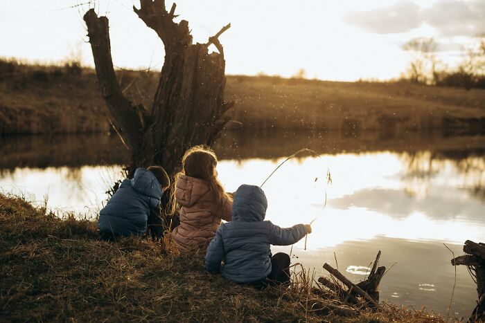 Three children sitting by a lake at sunset, capturing a peaceful moment amid chaotic and dramatic breakup stories.
