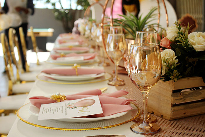 Elaborate wedding table setting with pink napkins, floral centerpieces, and elegant glassware in a bright venue.