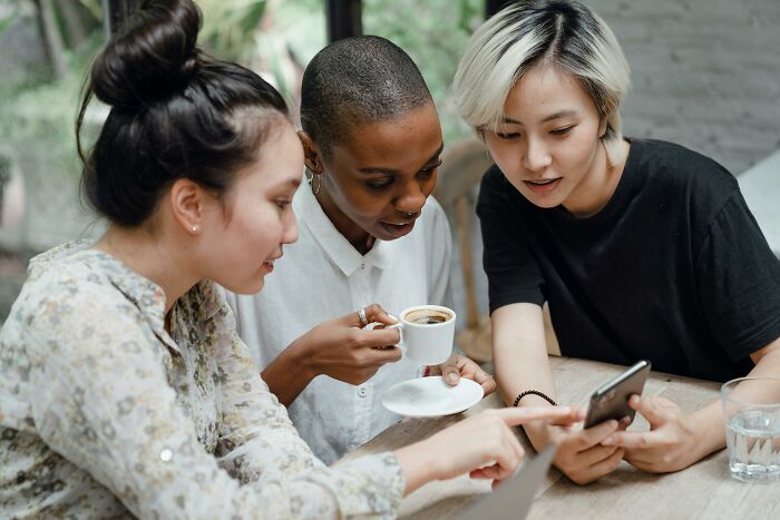 Three coworkers casually sitting together, discussing workplace rules while looking at a smartphone during a break.