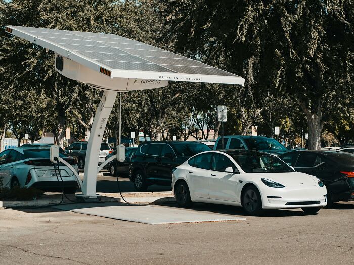 Solar-powered electric vehicle charging station with Tesla cars parked and charging in a sunny outdoor lot.