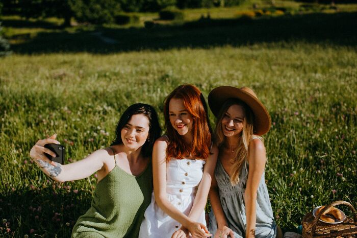 Three women sitting in a field taking a selfie, representing experience and advice in online dating.