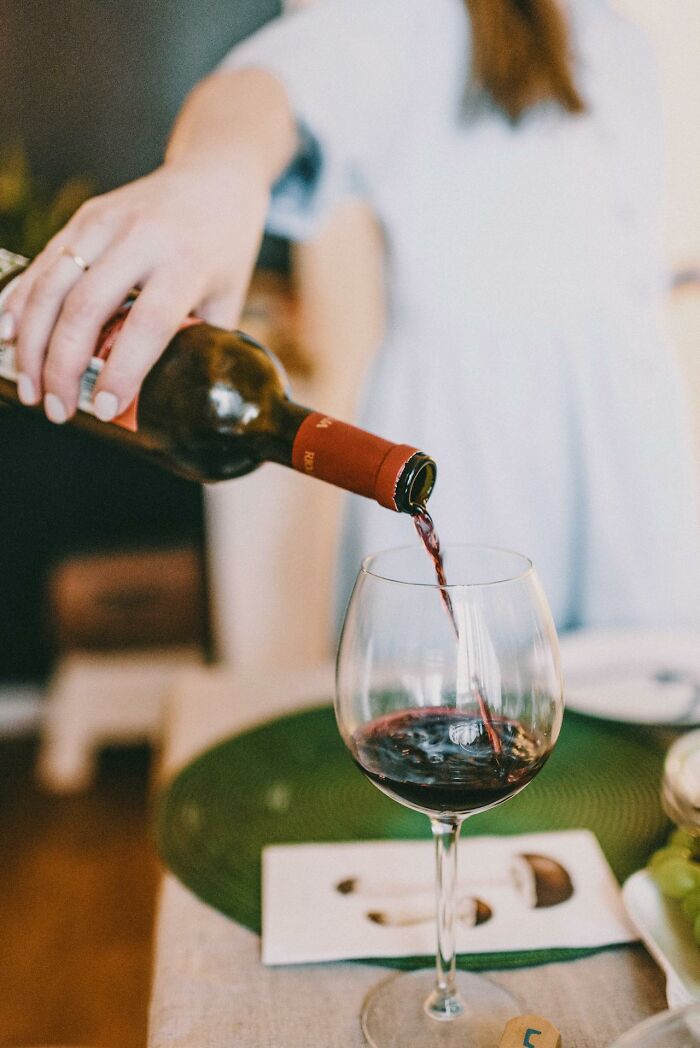 Person pouring red wine into a glass, capturing a casual moment of people embarrassed hilariously with drinks.