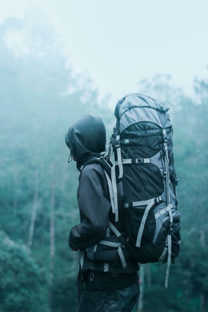 Person wearing a hood and carrying a large backpack in a foggy forest, appealing to true crime fans and adventurers.