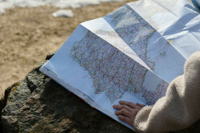 Person holding and studying a minimal map outdoors focusing on geography with cities and routes marked on the paper.