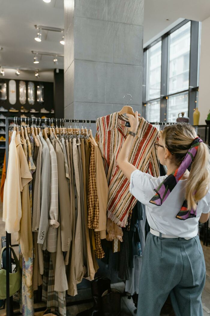 Woman shopping for clothes, holding a striped shirt in a store highlighting subtle sexist fashion norms for men.