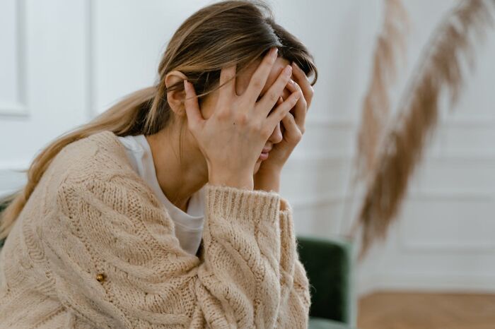 Woman in a beige sweater covering her face with hands, showing grief and distress related to worst and craziest funeral stories.