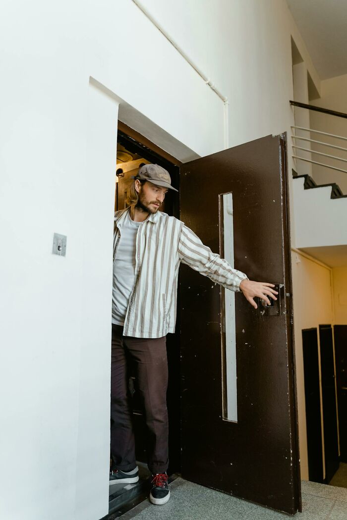 Man cautiously opening door in hallway, symbolizing suspicious behavior as a first sign someone is having an affair