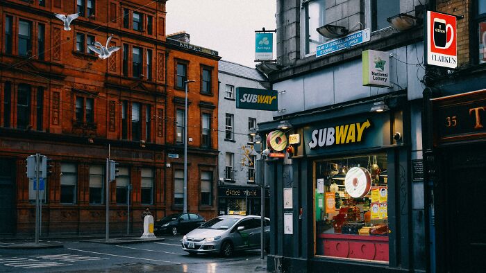 Subway restaurant exterior on a rainy day in an urban setting, illustrating tales from restaurant staff about unpaid bills.