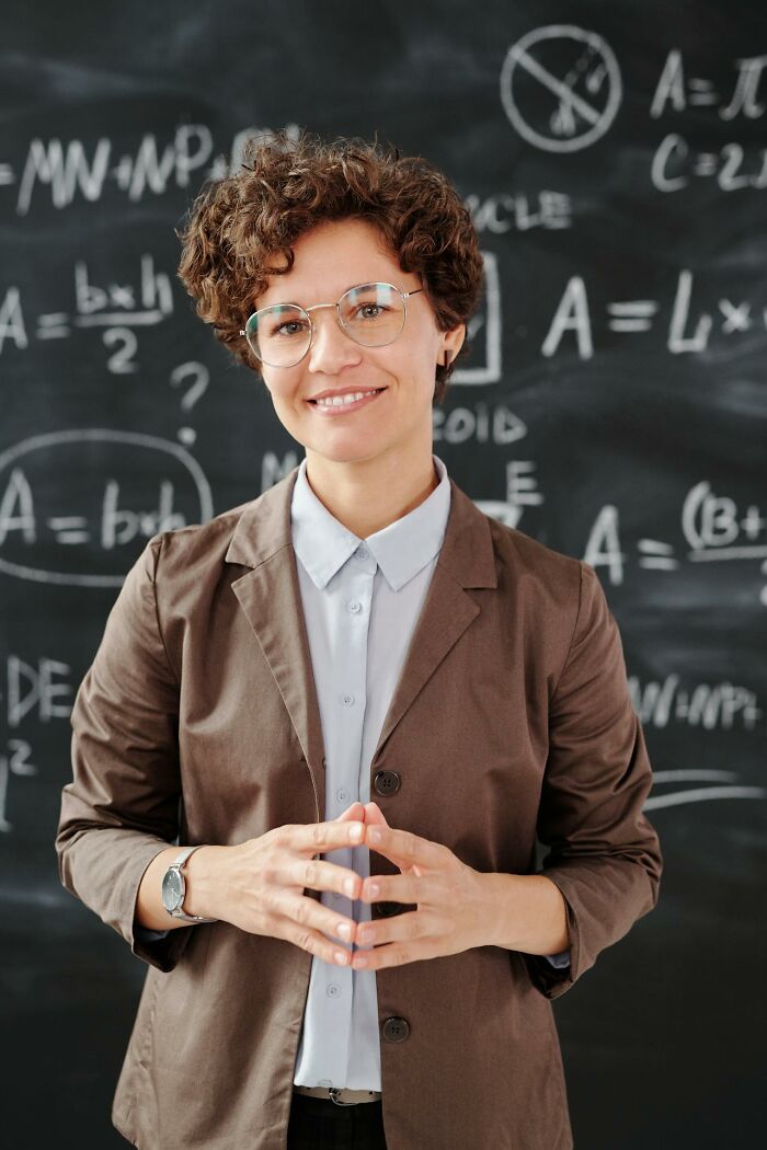 Person smiling, standing in front of a blackboard filled with chalk math formulas, illustrating karma striking with zero mercy.