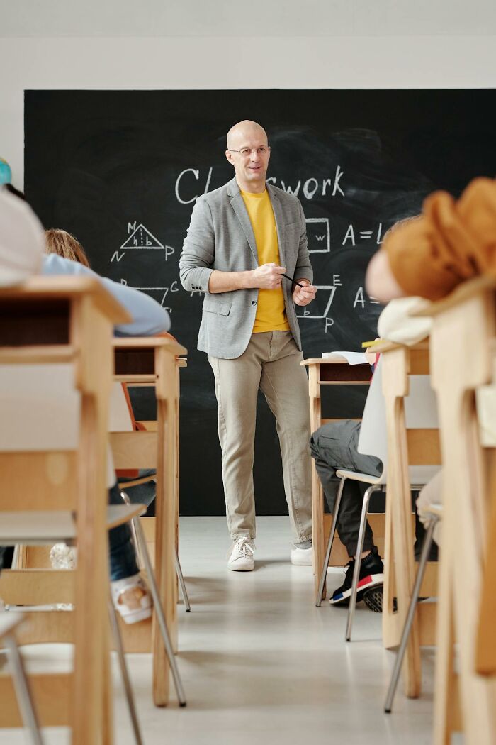 Teacher standing in front of a chalkboard with geometry formulas, engaging students in a classroom setting about karma stories.