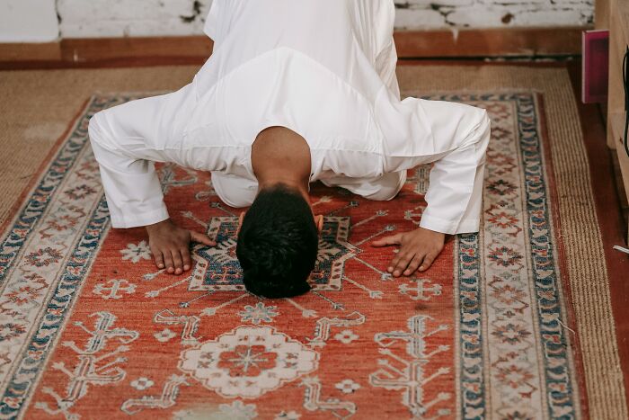 Man in traditional white clothing bowing down on a patterned rug, illustrating hilariously painful moments of misreading social cues.