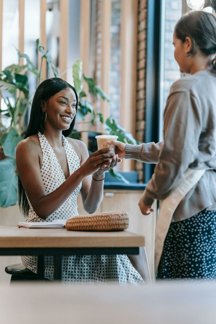 Woman smiling as she receives a drink from a server, a casual moment showing people embarrassed themselves so bad it's hilarious.