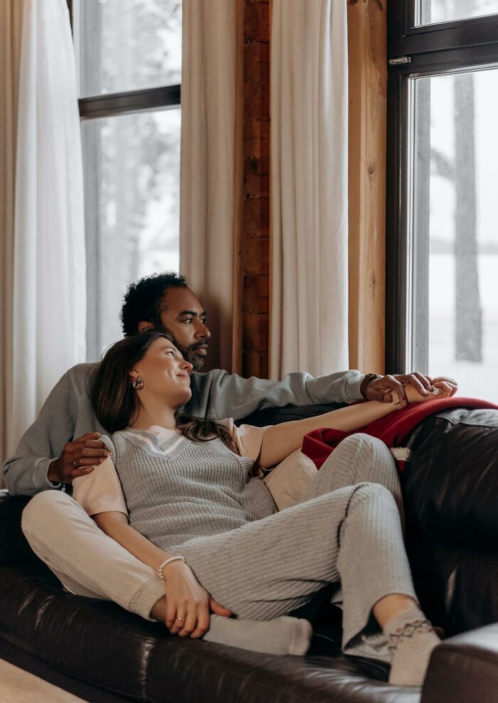 Couple sitting on a couch holding hands and looking out a window reflecting on how spouses changed after the wedding.