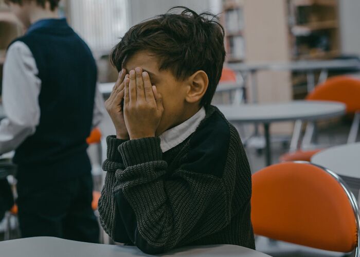 Young boy covering his face in a classroom setting, illustrating karma striking with zero mercy in daily life moments.