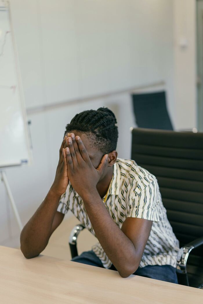 Young man sitting indoors with face in hands, expressing stress and regret about ignoring marriage red flags.