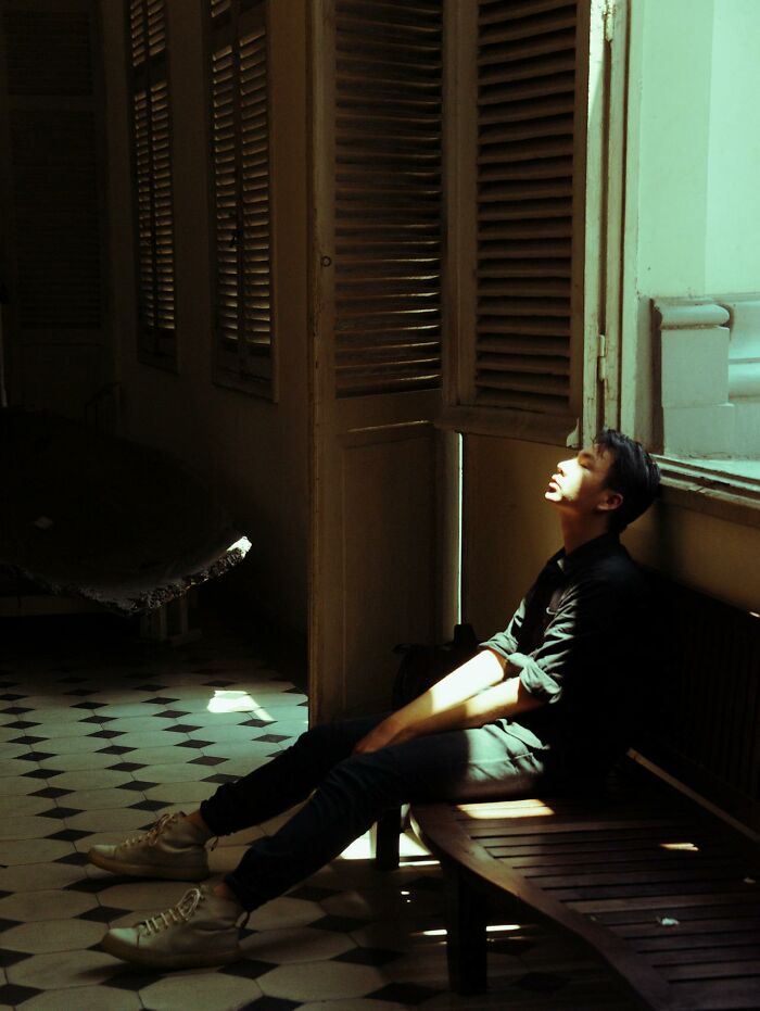 Young man sitting on bench in dim room with sunlight on face, reflecting on online dating experience advice insights.