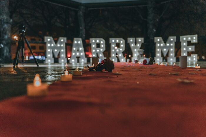 Romantic proposal setup with illuminated Marry Me sign, candles, and roses symbolizing dramatic breakup stories.