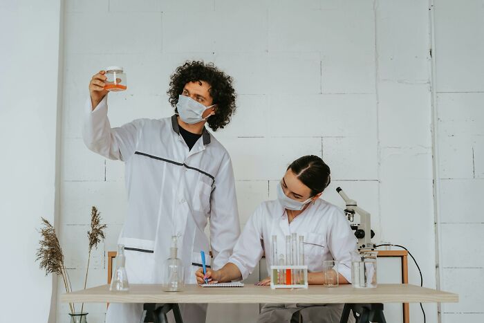 Two scientists wearing masks sharing potentially dangerous situations while examining samples in a lab setting
