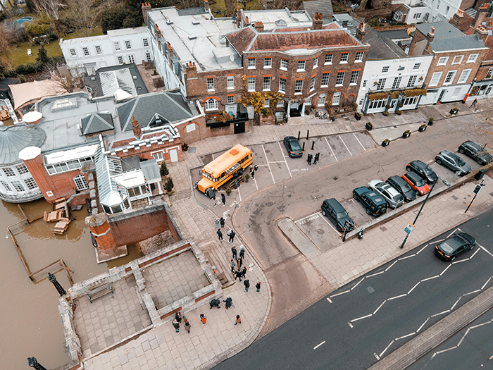 Aerial view of a group near a yellow school bus by historic buildings, emphasizing mom expected to put autistic student's needs first.