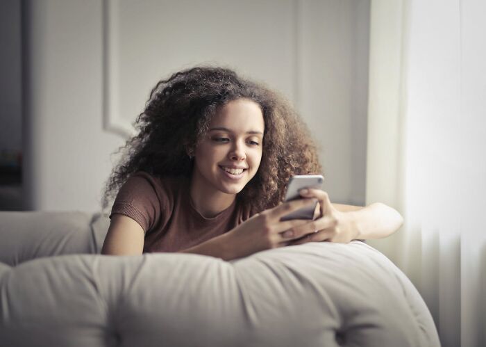 Young woman smiling while looking at her phone, illustrating signs someone is having an affair in a casual setting.