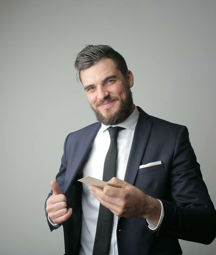 Man in dark suit and tie smiling while holding cards, representing unusual and crazy funeral stories.