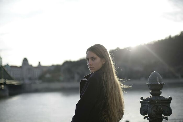 Young woman with long hair standing by a riverbank at sunset, reflecting on spouses changing after the wedding and red flags ignored.