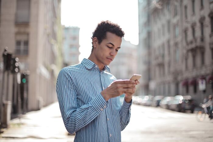 Young man in a striped shirt using phone outdoors, representing advice from people with experience in online dating.