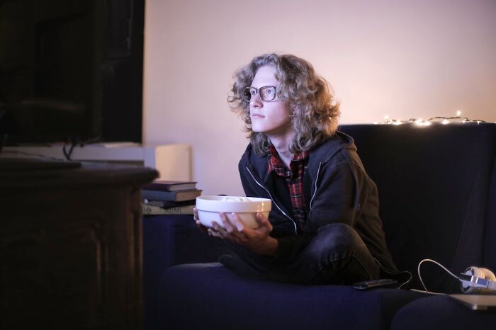 Young true crime fan watching TV intently, sitting on a couch with a bowl of popcorn in a dimly lit room.