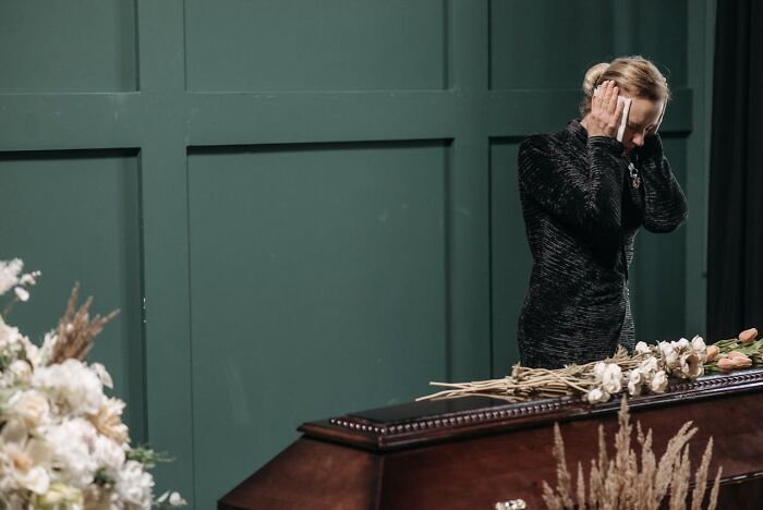 Woman in black mourning attire standing beside a coffin with flowers, illustrating funeral stories and experiences.