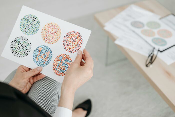 Person holding a color blindness test card with multiple circles of colored dots for vision assessment.