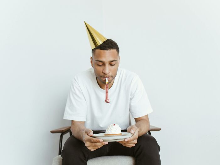 Young man wearing a party hat holding a plate with cake, looking down reflecting on dramatic breakup stories.
