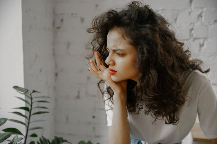 Woman with curly hair looking thoughtfully out a window, reflecting on chaotic breakup stories and emotional moments.