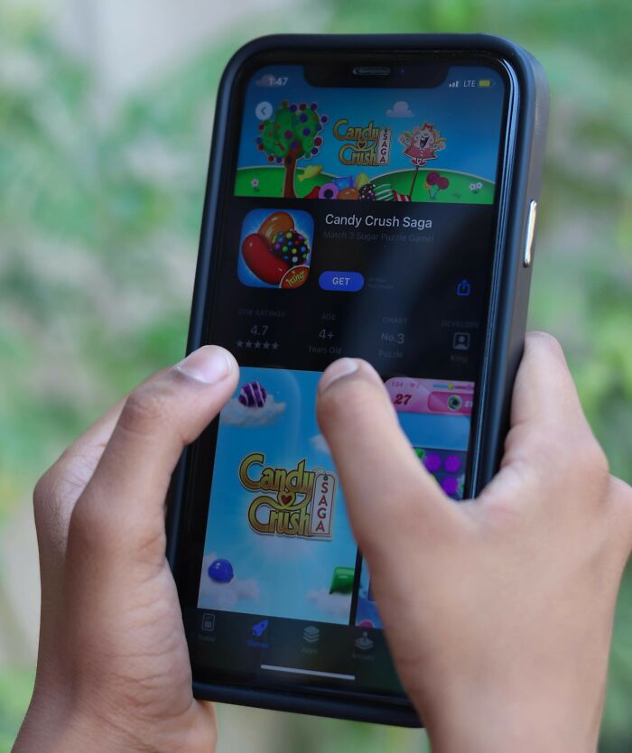 Hands holding a smartphone with a Candy Crush game screen, illustrating parents being bad at technology skills in a funny context.