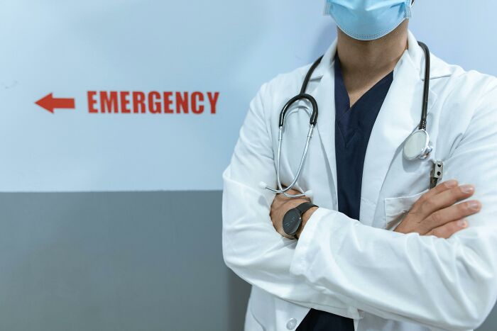 Doctor in white coat with stethoscope standing near emergency sign representing people share potentially dangerous situations.