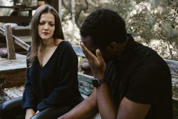 A conflicted couple sitting outdoors, showing emotions after a chaotic and dramatic breakup conversation.