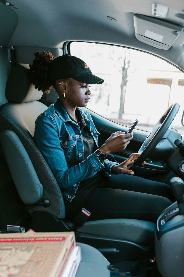 Young woman in a denim jacket using smartphone while sitting in a parked car, showing a moment of karma striking life event.