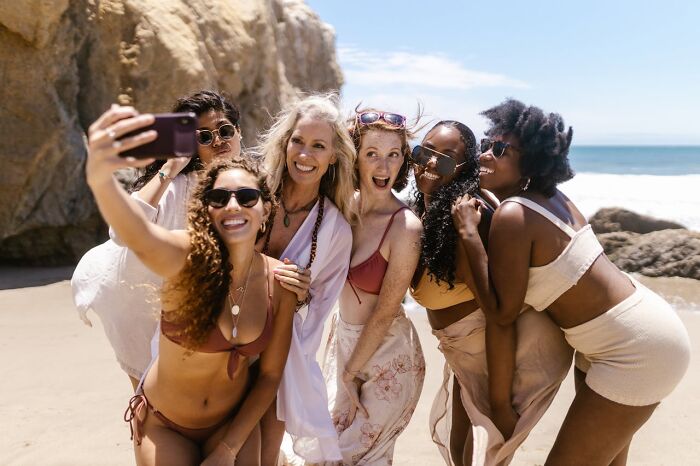Group of women at the beach taking a selfie, smiling and having fun, illustrating online dating experience advice concepts.