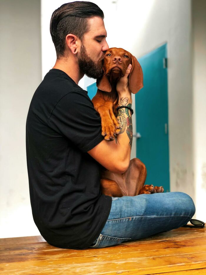 Man with tattoos sitting and kissing his dog, symbolizing secrets people are hiding from their partners forever.