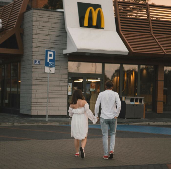 Couple walking hand in hand near a McDonald's entrance, illustrating women confessing unhinged stalking stories.