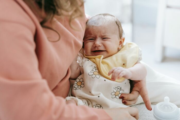 A clueless dad trying to soothe a crying baby in a floral onesie wearing a yellow bib during early parenting moments.