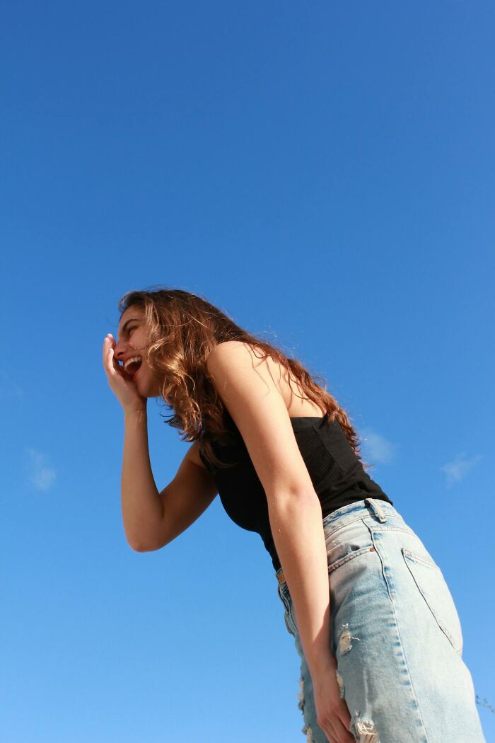 Young woman laughing outdoors under clear blue sky, representing heartbreak and broken trust by close friends.
