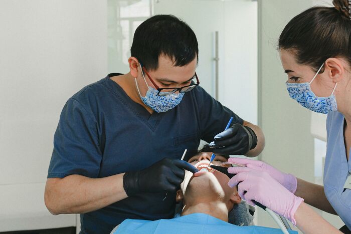 Two medical professionals wearing masks perform dental treatment highlighting effects of medical neglect affecting patients today