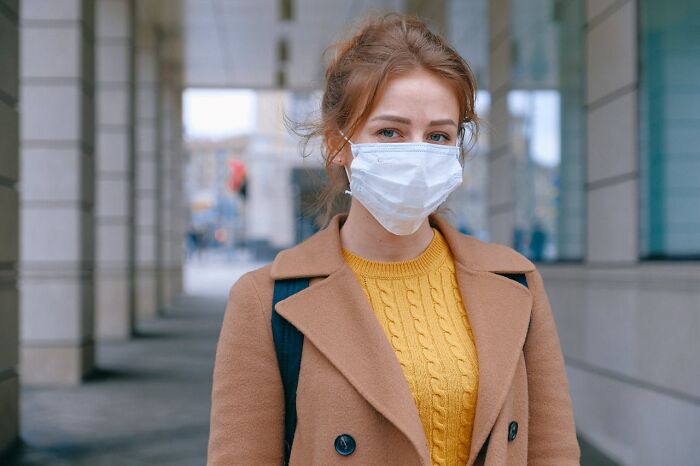 Young woman wearing a face mask and brown coat, reflecting on heartbreaking things committed by close friends that broke trust.