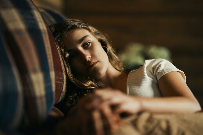 Young woman lying on a couch looking pensive and somber, reflecting on dark secrets that could ruin lives if revealed.