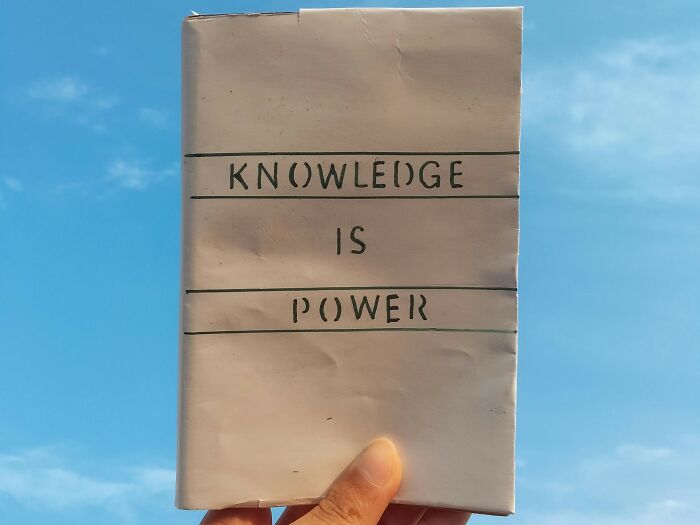 Hand holding a book with the proverb knowledge is power against a clear blue sky for language lovers.