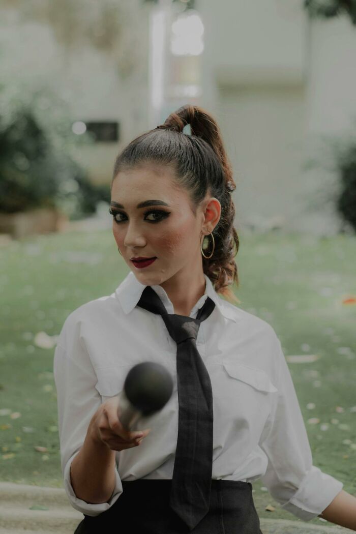 Young woman in a white shirt and black tie holding a microphone, highlighting subtle sexism and gender bias issues.