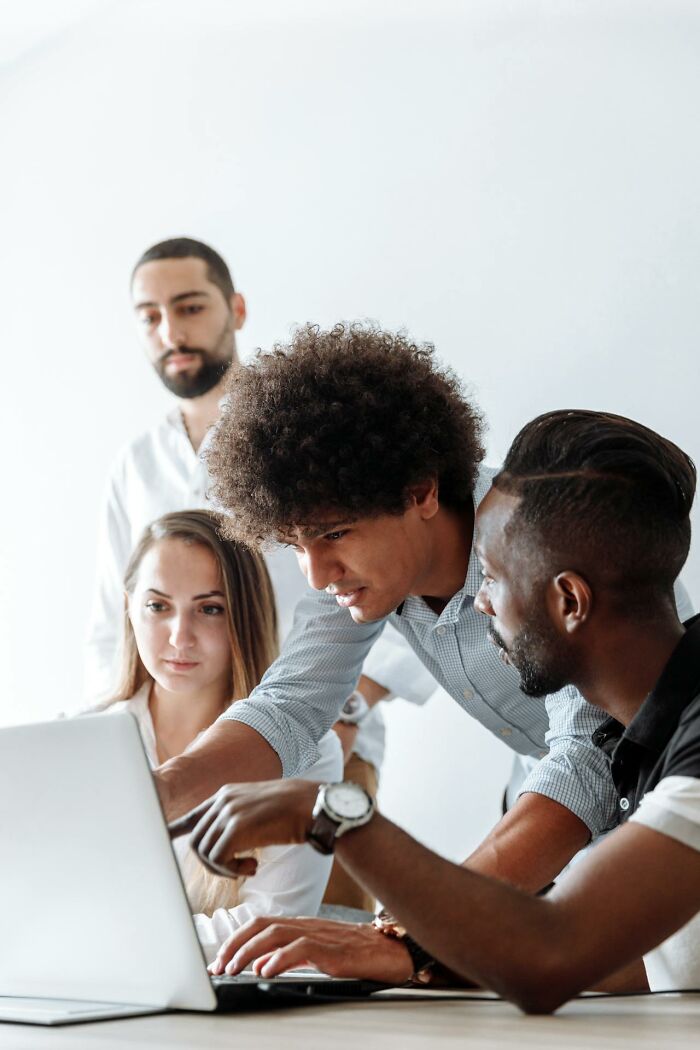 Diverse group of men collaborating and discussing work on a laptop, highlighting sexism awareness and gender issues.
