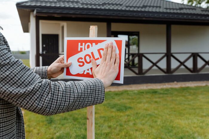 Person placing sold sign over home sale sign in front of house, symbolizing shocking dark secrets affecting lives.