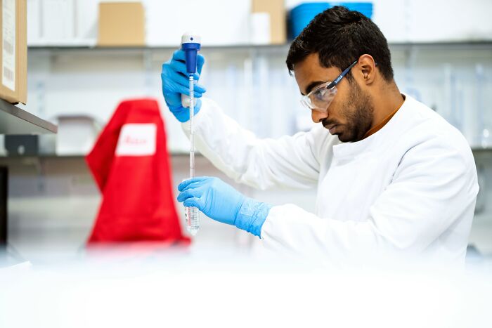 Healthcare worker in lab coat and gloves using a pipette in a laboratory setting, focused on precise measurements.